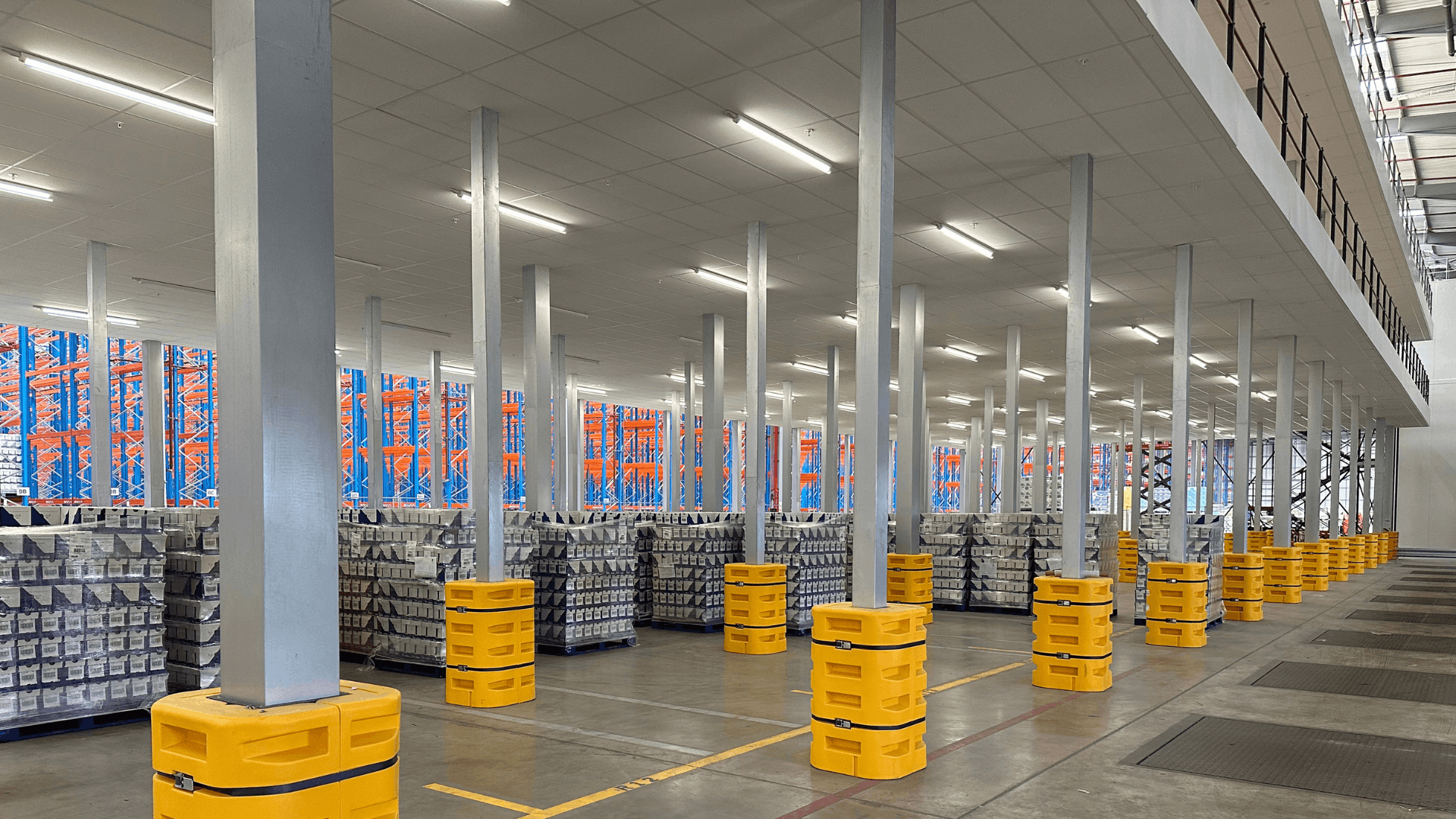 Under-mezzanine warehouse storage area at Ziegler with rows of steel columns, palletised stock, fire-rated ceiling and yellow column protection