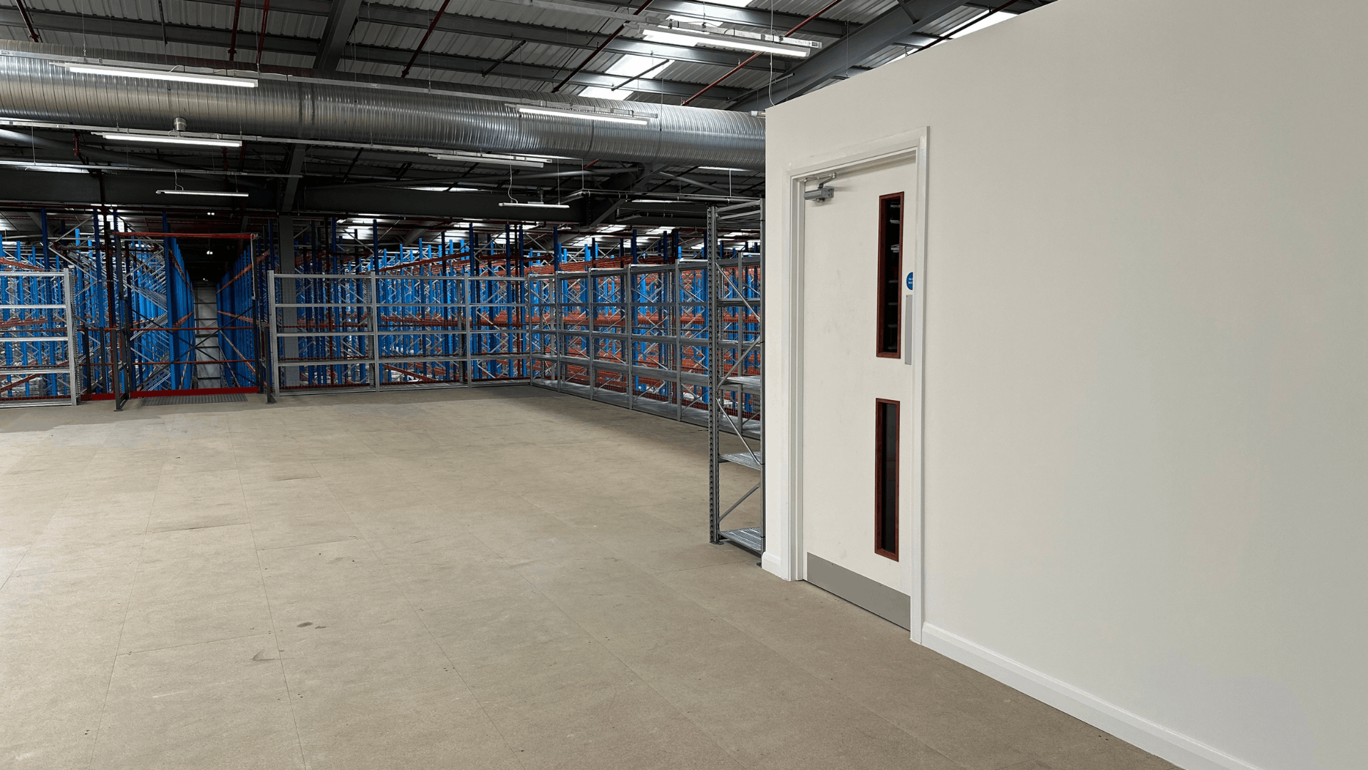 Upper mezzanine floor at Ziegler showing storage racking, fire-rated staircase enclosure with white door and open warehouse space beyond